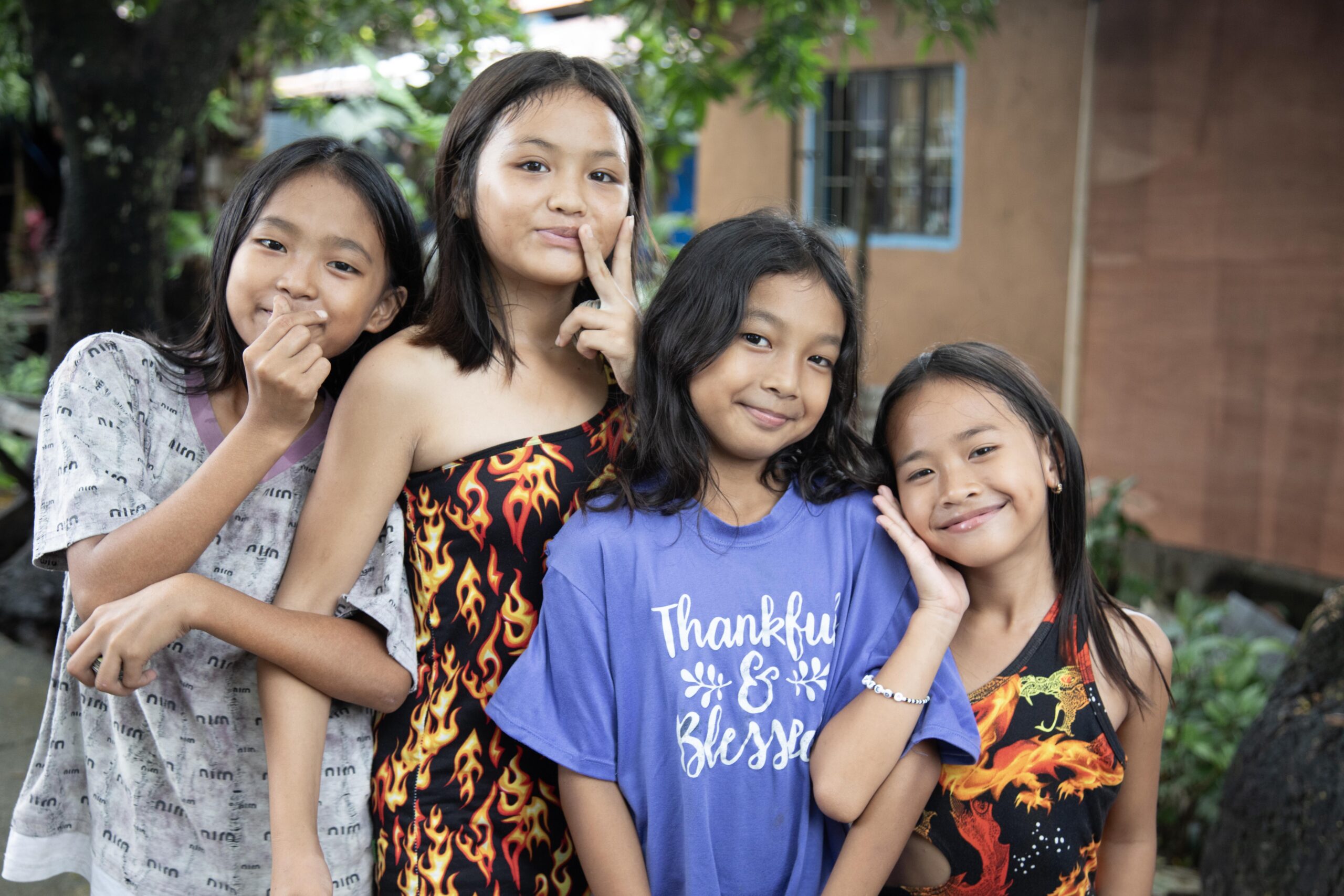 Four smiling girls pose together outdoors, showcasing their vibrant outfits and playful expressions.