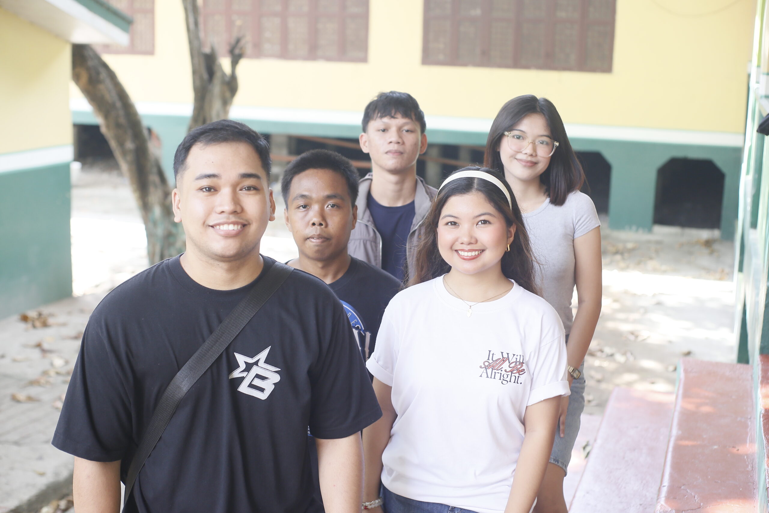 Five young adults smile together outdoors, showcasing friendship and camaraderie in a school setting.