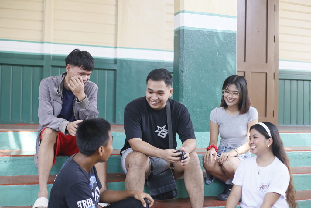 Five young adults sit on steps, laughing and engaging in conversation in a vibrant outdoor setting.
