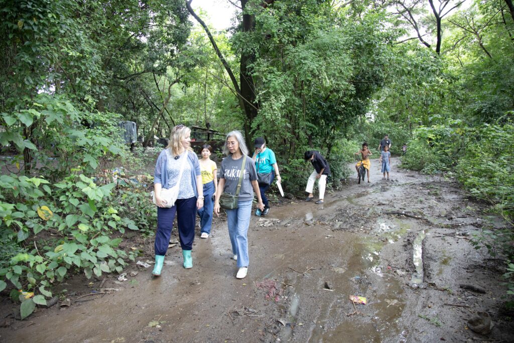 A group of people walks along a muddy path in a lush, green forested area, engaging in outdoor exploration.