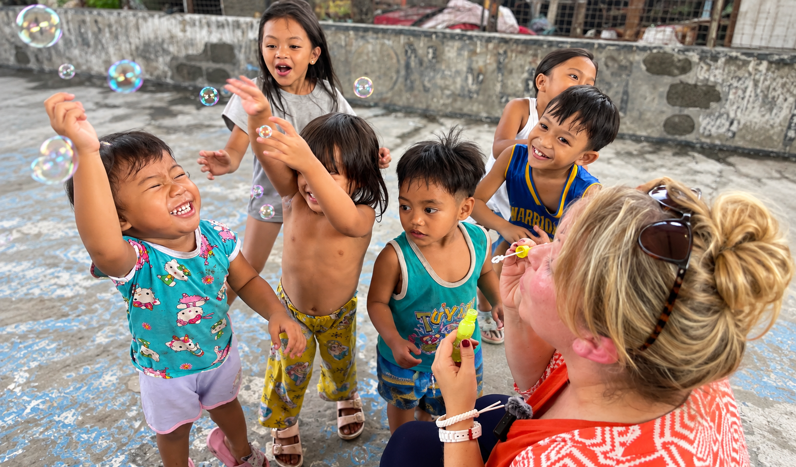 Children reach for bubbles as a woman blows them in a courtyard